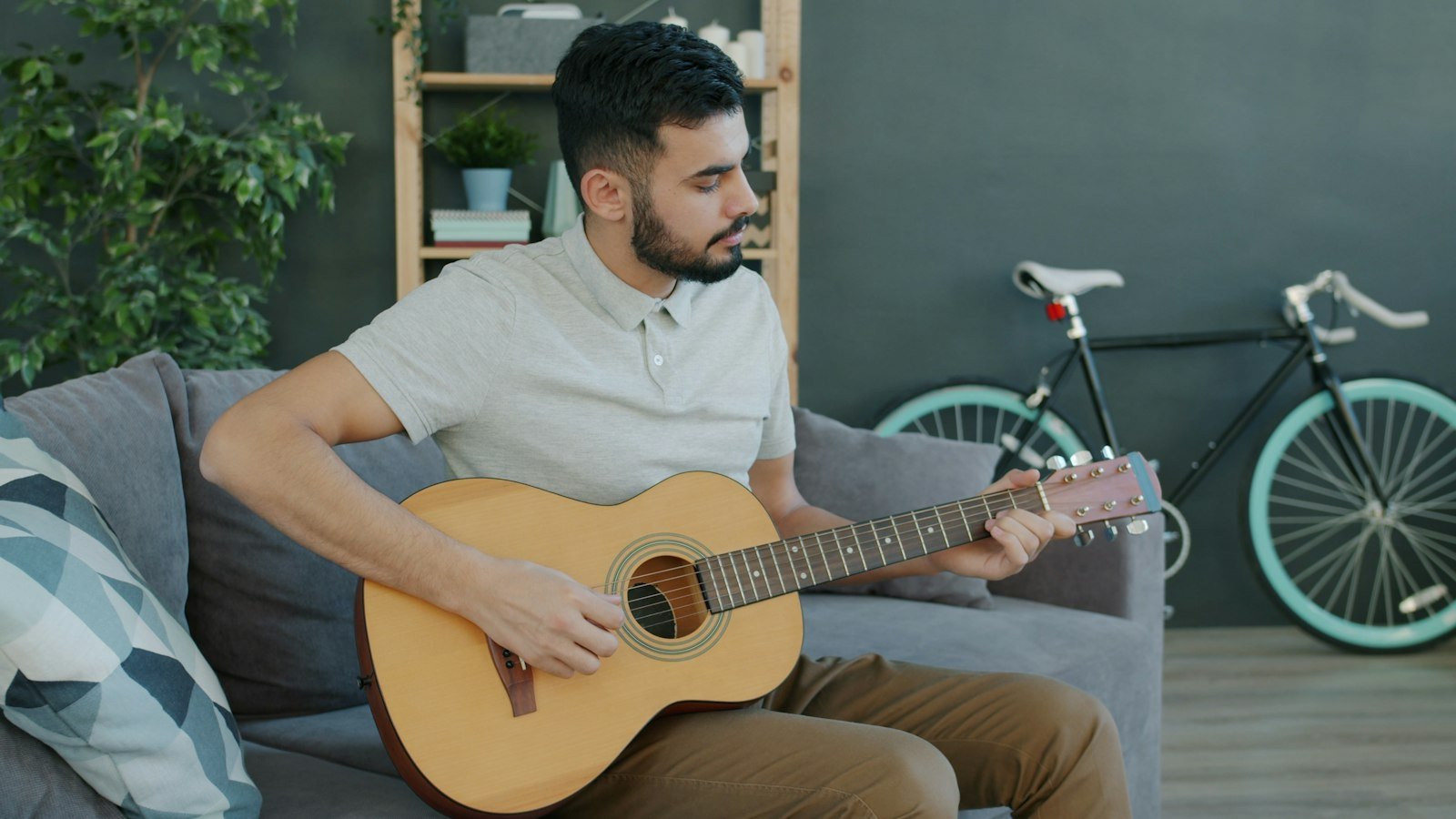 Man playing an acoustic guitar on a sofa at home