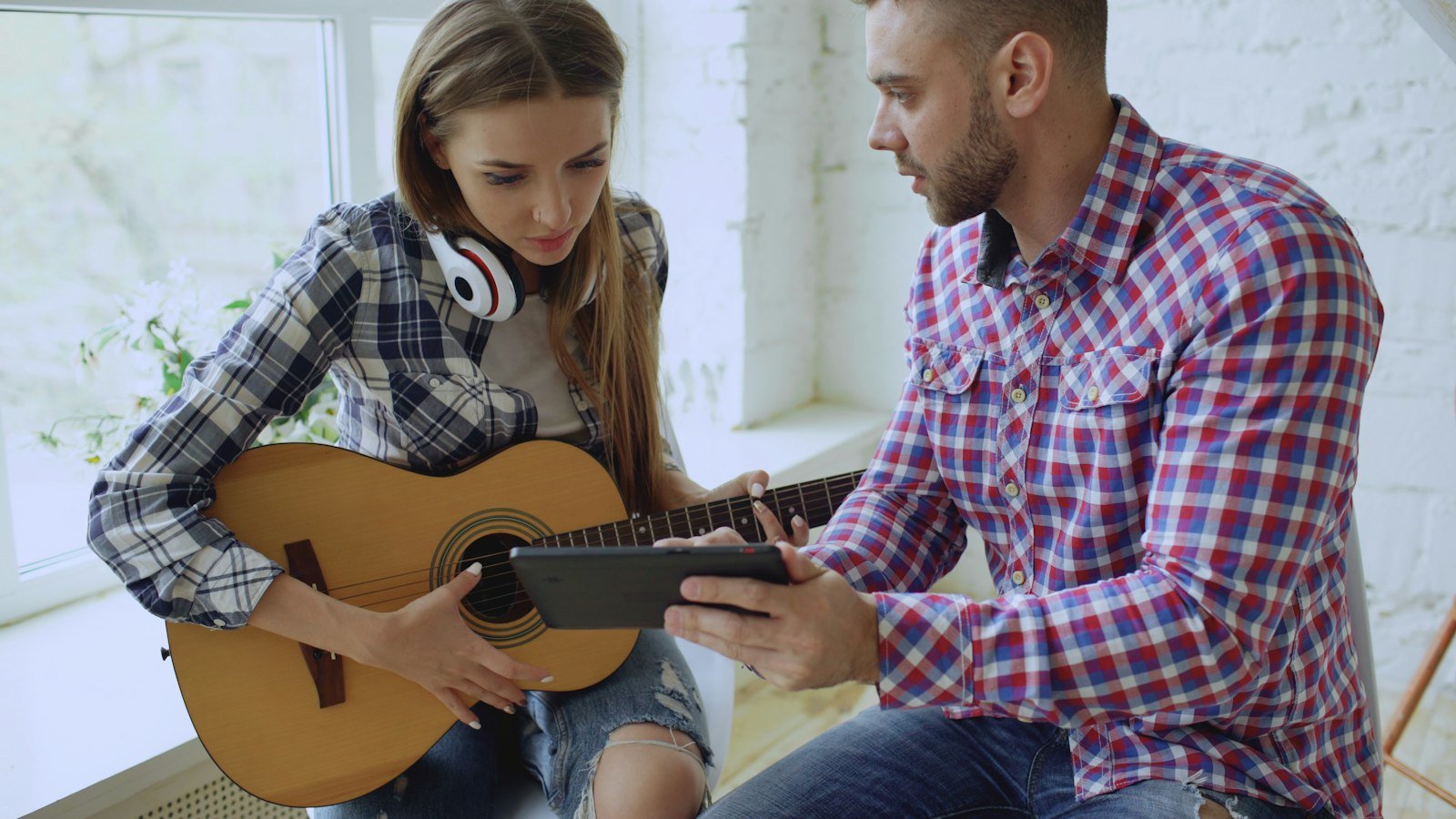 A man shows a woman holding a guitar something on a tablet